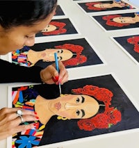 a woman painting frida kahlo portraits on a table